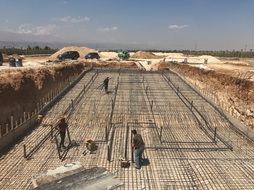 Wide view of swimming pool excavation with reinforcement and installed pipes